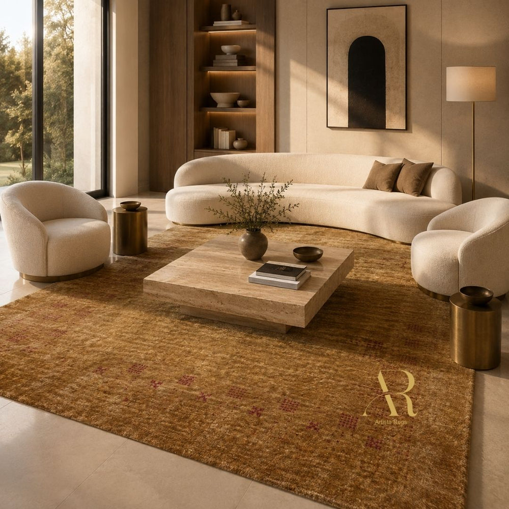 A large textured area rug in warm brown and gold tones with a stylized gold monogram, styled in a modern living room with cream curved sofas, a wooden coffee table, and warm ambient lighting.