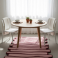 Round wooden dining table with chairs and decorative items in a bright room.