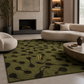 A green area rug with a black organic abstract pattern and a gold monogram 'R' in the center, styled in a modern living room setting.