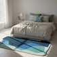 Modern bedroom with a bed and colorful rug on a wooden floor.