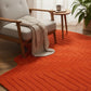 Orange rug with wavy pattern in a room with a chair and small table.