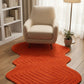 Orange textured rug on a wooden floor with a beige armchair and white bookshelf in the background.