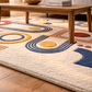 Colorful geometric-patterned rug on a wooden floor with a wooden coffee table in the background.