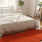 Orange rug on a wooden floor in a bedroom with a bed and plants.