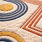 Close-up of a textured rug with circular and diagonal patterns in blue, orange, and beige.