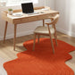 Wooden desk with laptop, chair, and orange rug on a light wood floor.