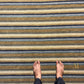 A top-down view of a striped area rug with horizontal bands of beige, brown, gray, and navy, with a person's bare feet standing on it.