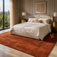 A large rust-orange area rug in a modern living room setting, styled with a curved cream sofa, two matching armchairs, a round stone coffee table, and tasteful decor.