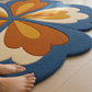 Colorful flower-shaped rug on a wooden floor with feet at the bottom.