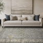 Beige sofa with decorative pillows on a patterned rug in a living room setting.