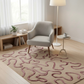 Living room with a gray armchair on a patterned rug, wooden shelf, and lamp.