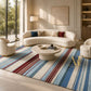 A luxury living room scene featuring a large area rug with blue, red, and cream stripes. The room is styled with a curved cream sofa, matching armchairs, a round stone coffee table, and elegant wall paneling.