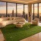 A luxury modern living room featuring a large green artificial grass rug with a gold monogram 'R' in the center, styled with a curved cream boucle sofa, a marble coffee table, and a matching accent chair, set against a backdrop of a city skyline at sunset.
