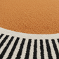Close-up of a round rug with orange, white, and black pattern