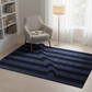 Blue striped rug in a room with a gray chair and white bookshelf.