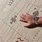 Close-up of a textured area rug with a cream-colored base, featuring a central rust-brown abstract symbol and scattered blue and gray motifs.