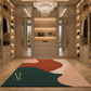A luxury walk-in closet interior with wood cabinetry, mirrors, a crystal chandelier, and a large abstract area rug in teal, coral, blush, and cream. A gold monogram logo reading AR is visible on the rug.