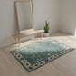 Teal patterned rug on a wooden floor with a mirror and plant in the background.