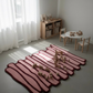 Pink and red striped rug with wooden toys on a light gray floor.