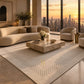 A modern luxury living room featuring a large cream-colored textured area rug with a dotted border pattern, a curved cream boucle sofa, a marble coffee table, and a stunning city skyline view at sunset through floor-to-ceiling windows.