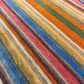 A close-up of a striped shag rug with thick diagonal bands of blue, red, orange, green, beige, and brown.