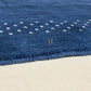 A dark navy blue rectangular rug with a textured surface, featuring a decorative border of small white dots and a gold monogram logo in the center, shown against a plain white background.