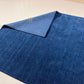 A dark blue textured area rug with a folded corner showing its lighter blue backing, placed on a light beige tiled floor.
