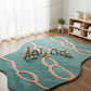 Teal and pink rug with toy blocks on a wooden floor in a room with white curtains.