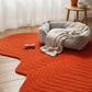Orange wavy-patterned rug with a pet bed and toys in a room with curtains and a small table.