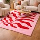 Living room with a pink rug featuring red abstract designs, a beige sofa, and a wooden coffee table.