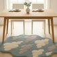 Dining table with chairs and a cloud-patterned rug in a bright room.