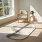 Round rug with wavy pattern on a wooden floor in a bright room with a chair and small table.