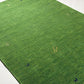 A green rectangular rug with a grass-like texture, featuring small embroidered motifs including a gold monogram and dark blue deer, shown on a light floor.