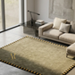Beige rug with a gold border and logo in a modern living room.