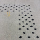 Close-up of a textured light beige rug with a repeating pattern of small black floral or clover-like motifs arranged in a curved row.