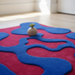 Red and blue abstract rug with a small plant on a wooden floor.