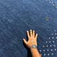 A dark navy blue rectangular rug with a textured surface, featuring a decorative border of small white dots and a gold monogram logo in the center, shown against a plain white background.
