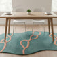 Dining table with chairs and a teal rug with pink patterns in a room.