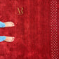 A red textured rug with a gold 'Anka Rug' logo near the top and a white diamond-patterned border on the right, shown with bare feet and blue jeans at the bottom left to indicate scale.