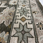 Close-up of a patterned rug with geometric designs and a brand logo.