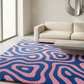 Modern living room with a pink and blue patterned rug, beige sofa, and large window.
