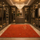 A luxurious walk-in closet with dark wood cabinetry, glass doors, and a large red area rug with a gold monogram in the center, under a crystal chandelier.