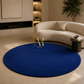 A round deep blue area rug with a gold 'Artisa Rugs' logo in the center, styled in a modern living room setting with a curved cream sofa and beige walls.