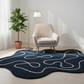 Modern living room with a blue abstract rug, beige armchair, and potted plant.