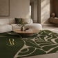 A green and beige patterned area rug styled in a modern, minimalist living room with a white curved sofa and a round wooden coffee table.