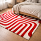 Red and white patterned rug on a wooden floor in a bedroom setting.