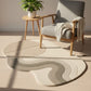Round rug with wavy pattern in a room with a chair, side table, and plant.