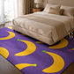 A purple area rug with a bold yellow banana pattern, styled in a modern bedroom setting under a beige bed.