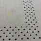 A close-up of a light beige textured rug with a repeating pattern of small black floral or leaf-like motifs arranged in diagonal rows.