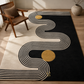 A modern area rug with a black background, cream-colored concentric wavy lines, and two gold circles, styled in a minimalist room next to a wooden armchair.